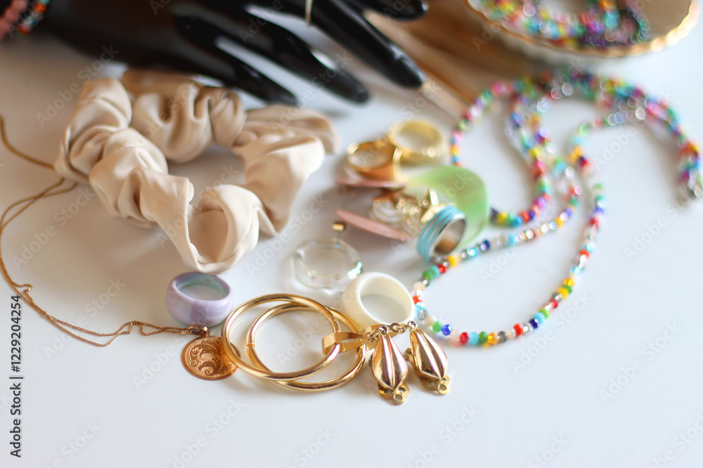 Hand figurine, sunglasses, gold jewelry, colorful bead jewelry, statement rings and various hair accessories on the white table. Selective focus.