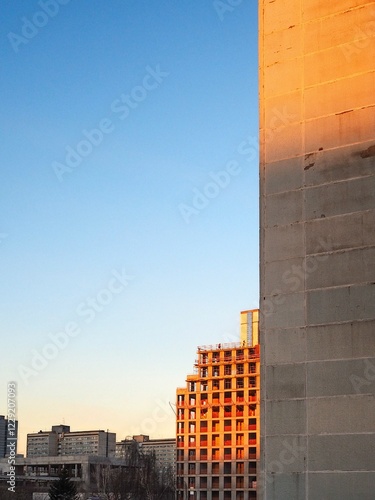 A fragment of a concrete building under construction in the orange light of the morning sun against the backdrop of a cloudless sky.