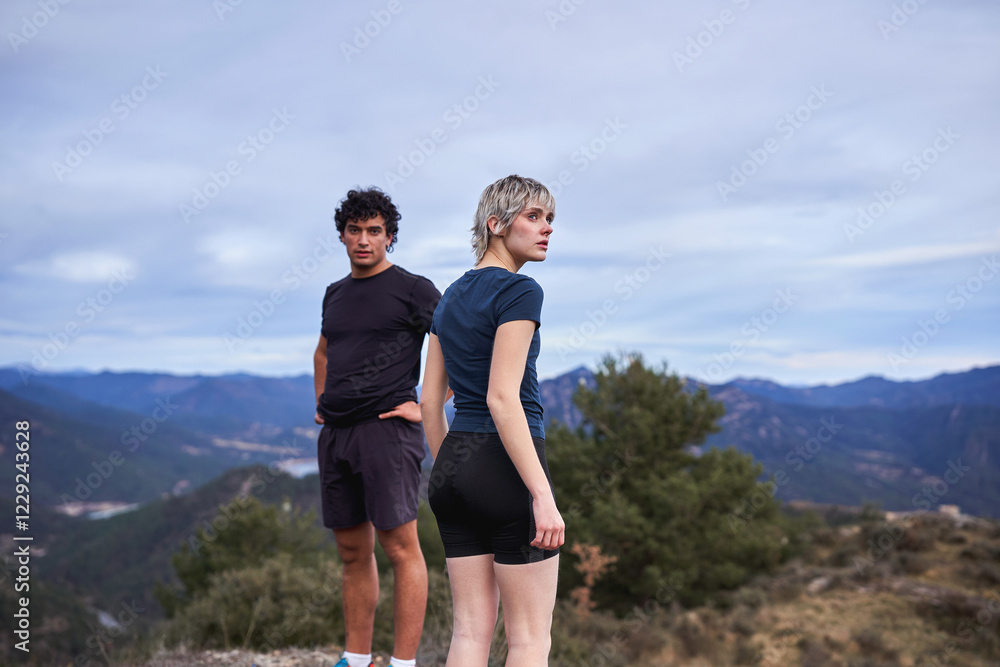 Obraz premium Two young hikers standing at the mountain summit, enjoying the scenic view