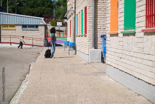 Wallpaper Mural Teacher standing outside school with trolley bag while student playing soccer in schoolyard Torontodigital.ca