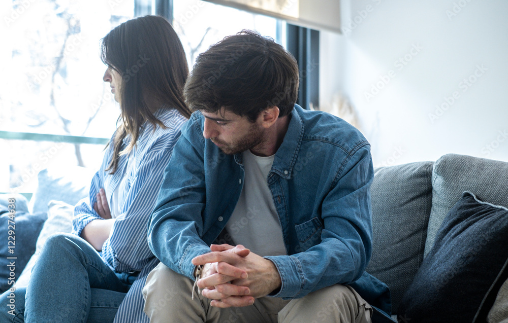 Man and woman sitting apart on a sofa in their living room, struggling with trust issues, emotional detachment, arguing, ignoring each other, feeling sad, and dealing with relationship problems Man and woman sitting apart on a sofa in their living room, struggling with trust issues, emotional detachment, arguing, ignoring each other, feeling sad, and dealing with relationship problems