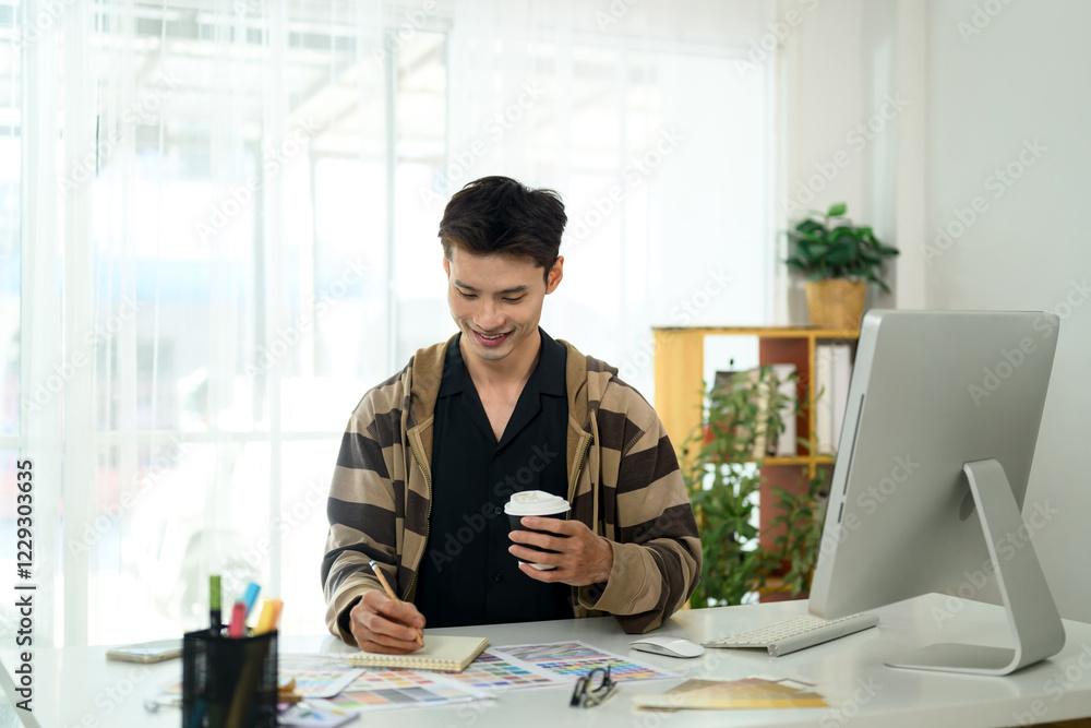 Smiling male designer working on a new project and sketching ideas on notepad Smiling male designer working on a new project and sketching ideas on notepad