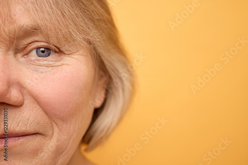 A woman with light blonde hair is smiling gently against a bright yellow backdrop. Her expression conveys warmth and kindness as she engages the viewer photo