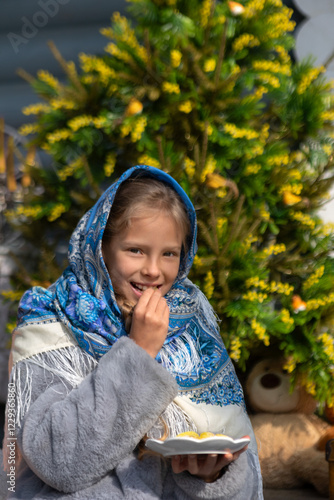 A beautiful Russian girl in a fur coat and headscarf sits on the porch of a wooden house on a sunny spring day. Family values, traditions and home comfort.Tea drinking outside the house