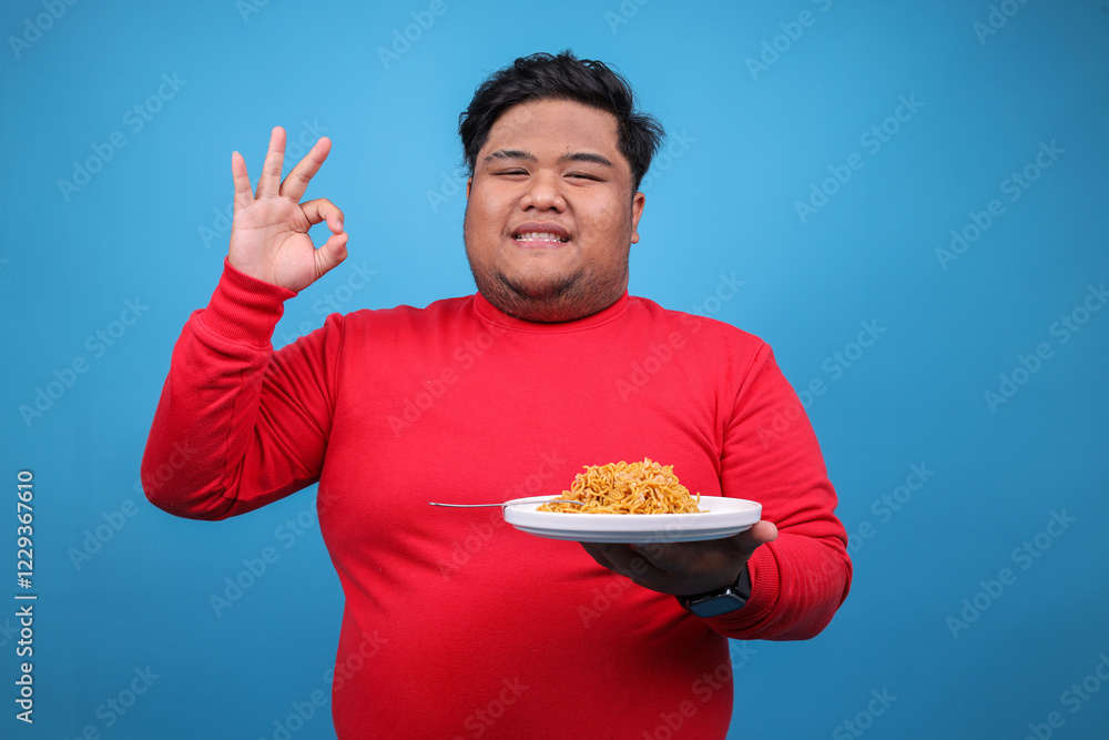 Portrait Of Cheerful Fat Man Showing OK Sign While Holding A Plate Of Fried Noodle Over Blue Background Portrait Of Cheerful Fat Man Showing OK Sign While Holding A Plate Of Fried Noodle Over Blue Background