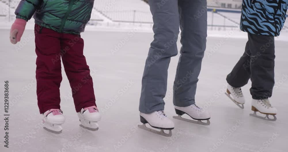 Mother helping two daughters ice skate on large outdoor stadium rink during winter, creating fun and memorable family moment. Mother helping two daughters ice skate on large outdoor stadium rink during winter, creating fun and memorable family moment.