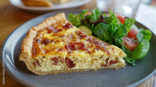 A fluffy slice of quiche Lorraine, with bacon and cheese, served with a simple side salad.