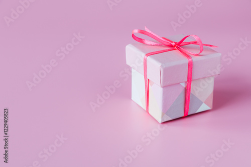 A gift box tied with a red ribbon with a bow on a pink background. The gift concept.