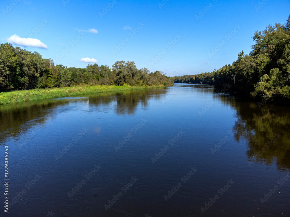 A calm river with trees on both sides. The water is clear and the sky is blue. The scene is peaceful and serene A calm river with trees on both sides. The water is clear and the sky is blue. The scene is peaceful and serene