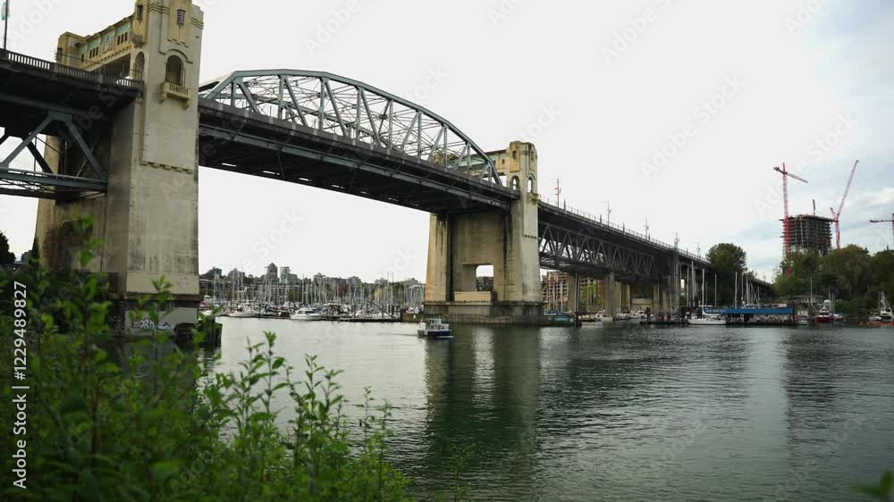 Small publit transit water taxi passes under Burrard Bridge in Vancouver on a quiet and calm day in the marina with cloud in the sky Small publit transit water taxi passes under Burrard Bridge in Vancouver on a quiet and calm day in the marina with cloud in the sky