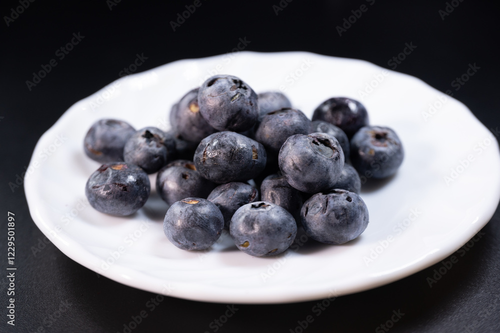 A macro shot of freeze-dried blueberries on a white dish, showing their wrinkled texture and deep blue color against a dark background. Great for food, nutrition, and healthy snack themes. A macro shot of freeze-dried blueberries on a white dish, showing their wrinkled texture and deep blue color against a dark background. Great for food, nutrition, and healthy snack themes.