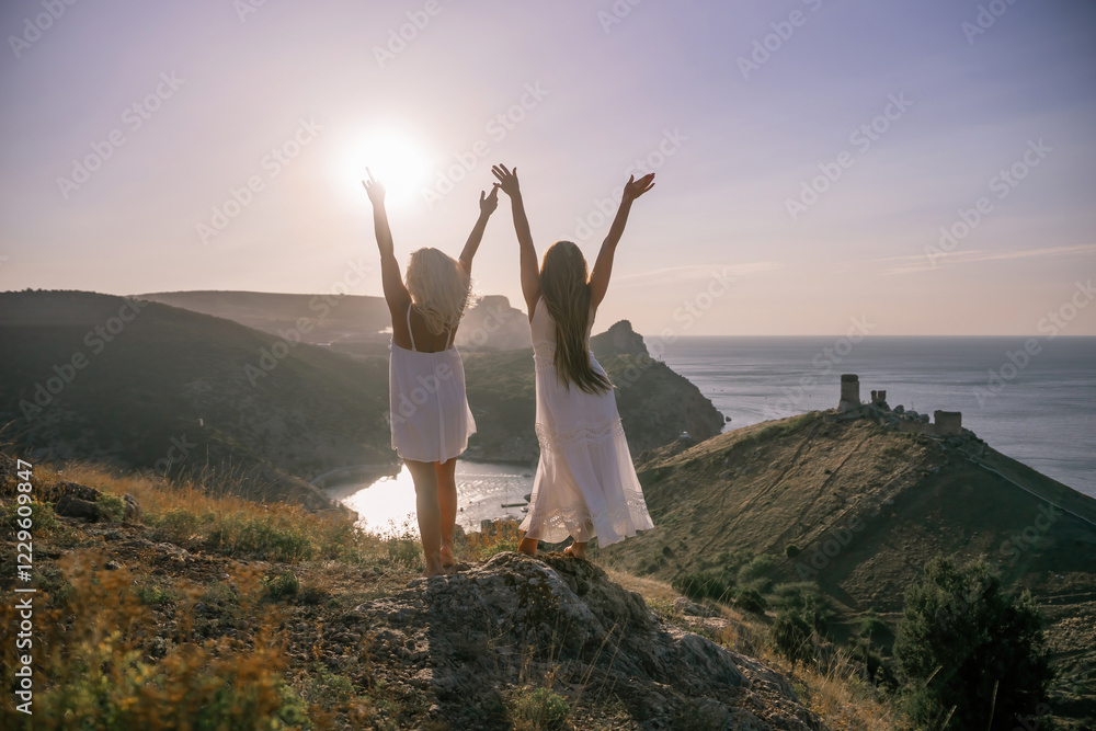 Two women are standing on a hill overlooking the ocean. They are holding hands and looking out at the water. The scene is peaceful and serene, with the sun shining brightly in the background. Two women are standing on a hill overlooking the ocean. They are holding hands and looking out at the water. The scene is peaceful and serene, with the sun shining brightly in the background.