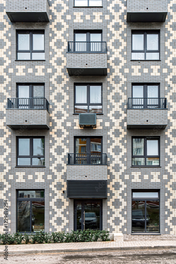 Fototapeta premium Modern building with a geometric brick pattern, featuring balconies with metal railings and windows, urban concept, front view