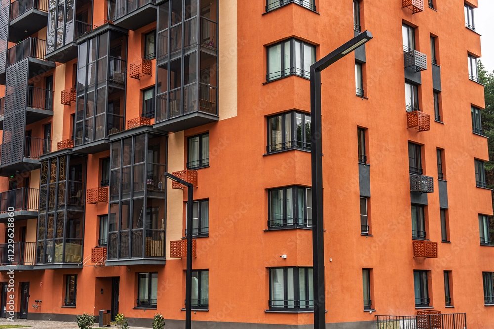 Obraz premium Contemporary apartment building with orange facades, featuring numerous balconies with dark-framed windows. Urban housing concept