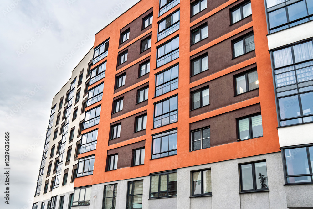 Modern apartment building facade, featuring beige, orange, and brown tones, with dark-framed windows, low angle view. Urban housing concept Modern apartment building facade, featuring beige, orange, and brown tones, with dark-framed windows, low angle view. Urban housing concept