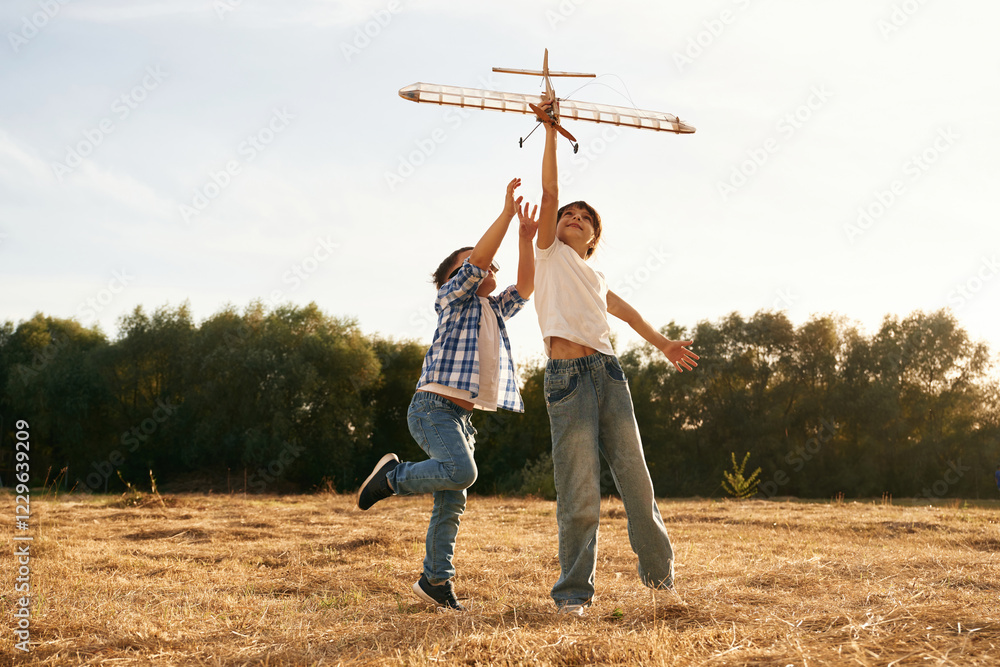 Fototapeta premium Flying high up. Boy and girl are playing with wooden toy plane on the field