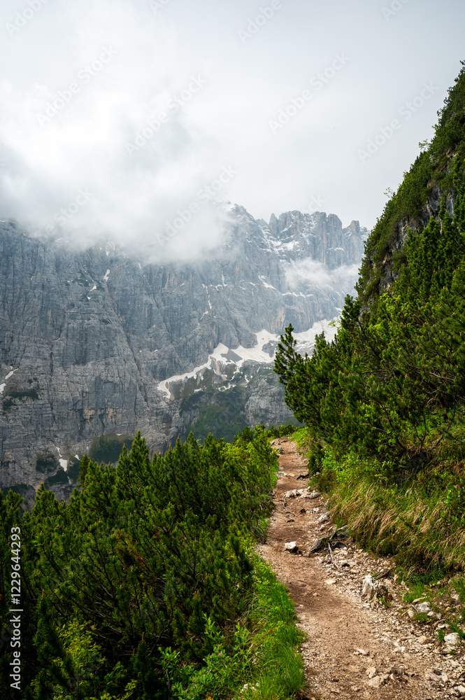 Mountain trail in the Dolomites (Dolomiti, Dolomiten), Italy, leading to Lago Sorapis. The path winds along rocky slopes with stunning views of valleys, forests, and peaks
