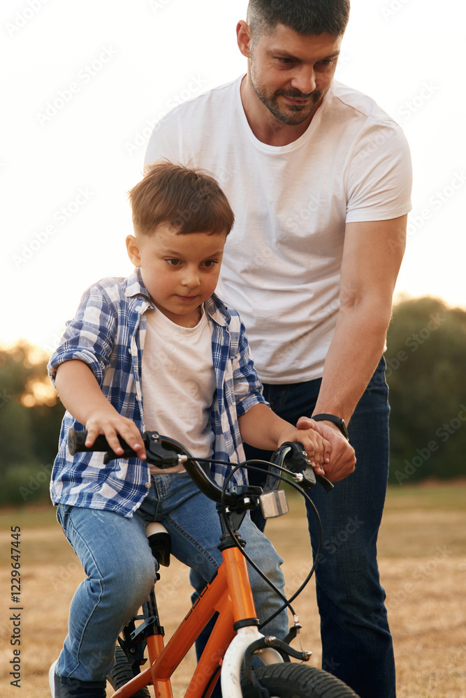 Teaching how to ride. Dad with son are with bicycle on the field outdoors Teaching how to ride. Dad with son are with bicycle on the field outdoors