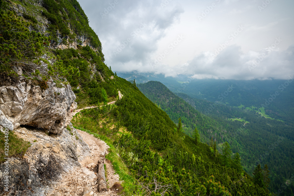 Mountain trail in the Dolomites (Dolomiti, Dolomiten), Italy, leading to Lago Sorapis. The path winds along rocky slopes with stunning views of valleys, forests, and peaks