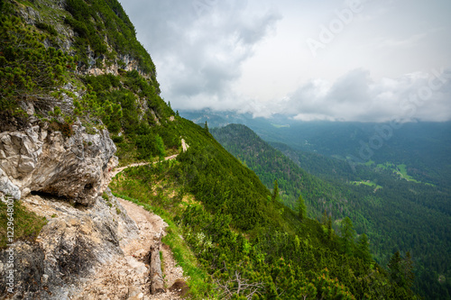 Obraz na płótnie Mountain trail in the Dolomites (Dolomiti, Dolomiten), Italy, leading to Lago Sorapis. The path winds along rocky slopes with stunning views of valleys, forests, and peaks w salonie