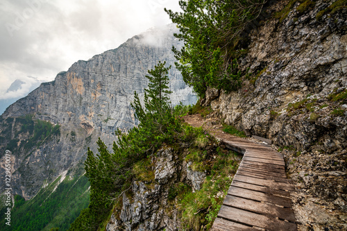 Mountain trail in the Dolomites (Dolomiti, Dolomiten), Italy, leading to Lago Sorapis. The path winds along rocky slopes with stunning views of valleys, forests, and peaks