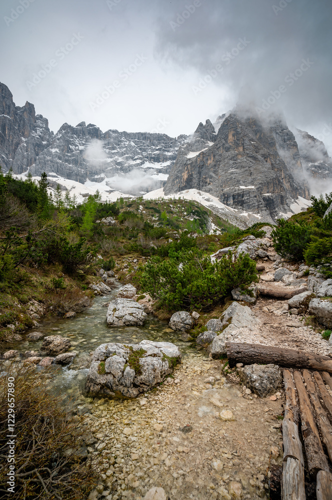 Rocky hiking trail near Lago Sorapis in the Dolomites (Dolomiti, Dolomiten), Italy. The path runs alongside a small mountain stream, with massive boulders and peaks in the background