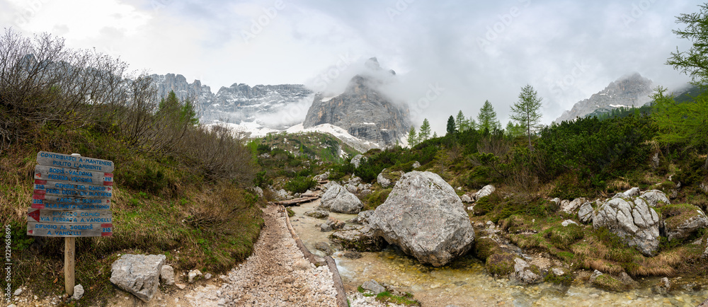Rocky hiking trail near Lago Sorapis in the Dolomites (Dolomiti, Dolomiten), Italy. The path runs alongside a small mountain stream, with massive boulders and peaks in the background