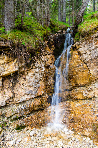 Obraz na płótnie Small waterfall cascading down a rocky cliff in a lush forest of the Dolomites (Dolomiti, Dolomiten), Italy. The fresh water flows over moss-covered stones in nature w salonie
