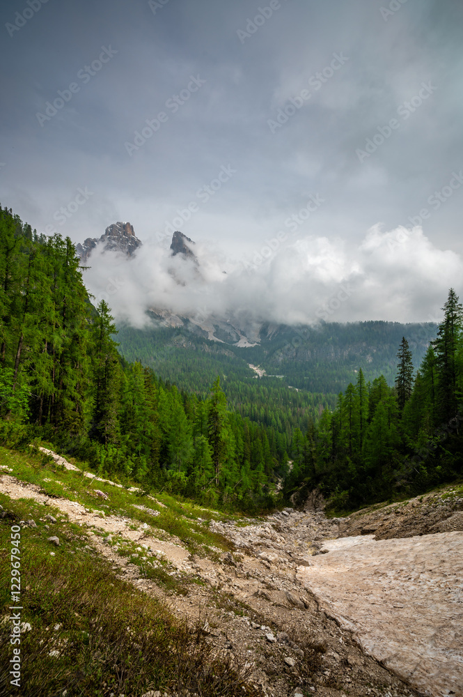 Mountain trail in the Dolomites (Dolomiti, Dolomiten), Italy, leading to Lago Sorapis. The path winds along rocky slopes with stunning views of valleys, forests, and peaks