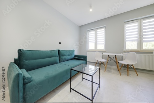 Salon w nowoczesnym apartamencie z seledynowym aneksem kuchennym z ciemnozieloną sofą photo