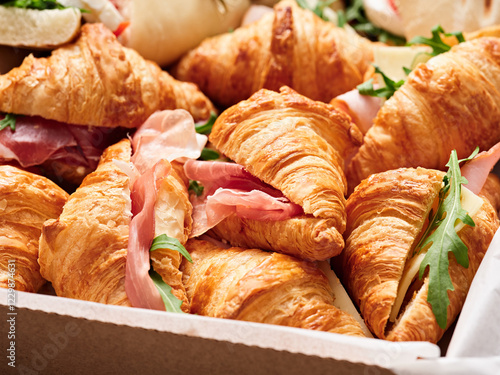 A tray filled with golden-brown croissants stuffed with slices of ham and fresh arugula, perfect for a breakfast or brunch occasion, inviting and delicious photo