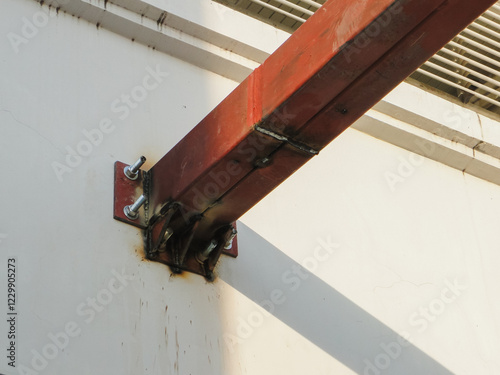 The base plate is secured to a concrete surface with six bolts, three on each side of the column. The steel column is painted red and is welded to the base plate. photo