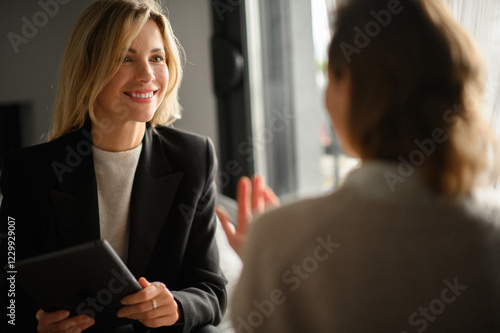 A businesswoman smiling and engaging in a face-to-face conversation with a client, listening attentively and explaining, reflecting professionalism and friendly communication.