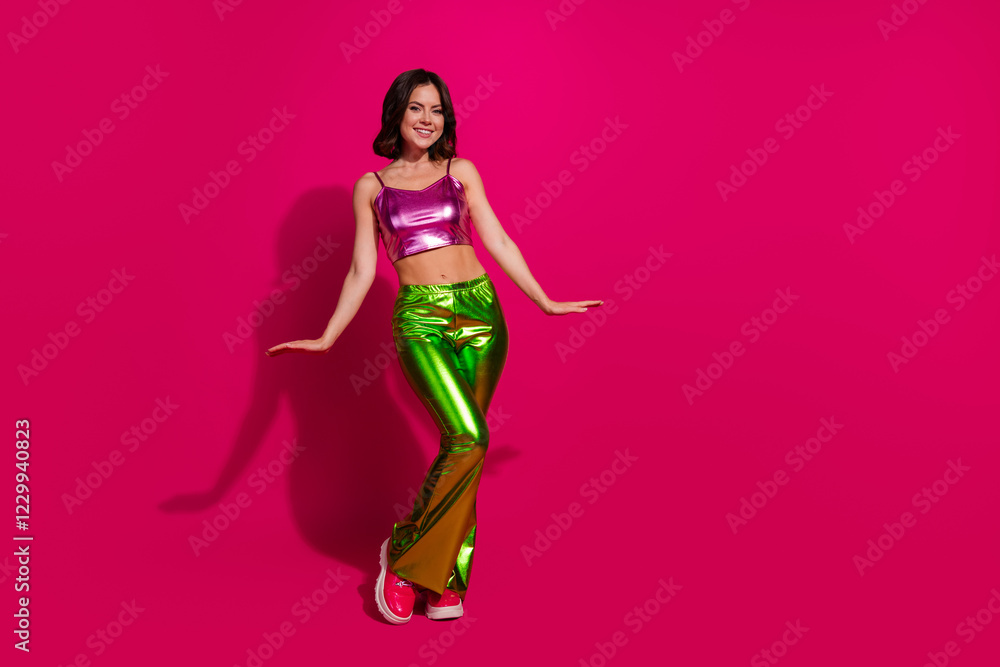 Stylish young woman in bright glossy clothing dancing against vivid magenta background Stylish young woman in bright glossy clothing dancing against vivid magenta background