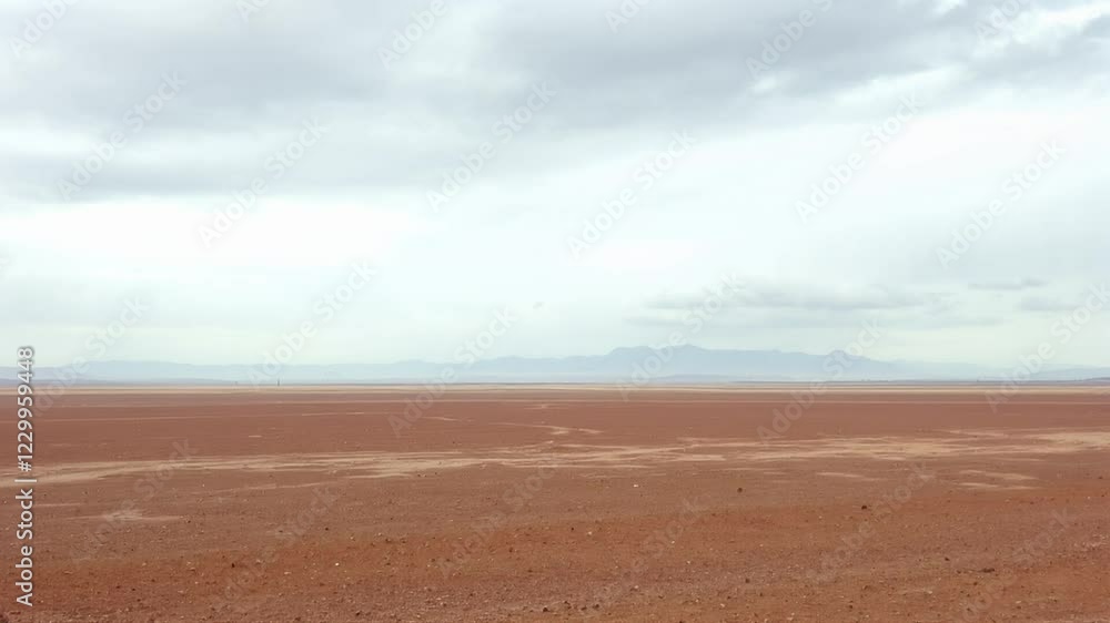 Red desert landscape under overcast sky, distant mountains Red desert landscape under overcast sky, distant mountains