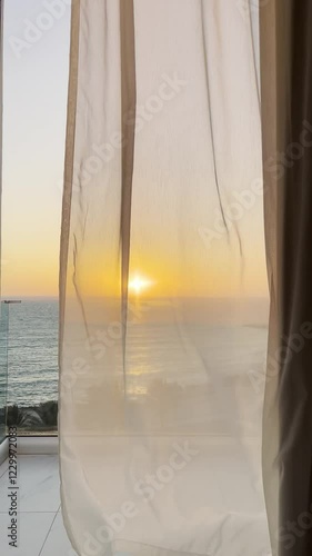 vertical video of colourful sunset golden hour from a hotel transparent glass balcony to Mediterranean Sea of greek cyprus island with curtains moving in the wind