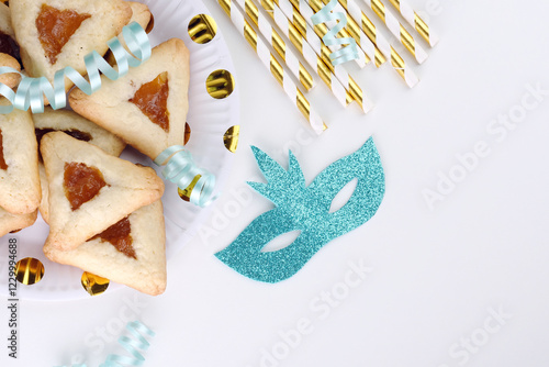 Close up freshly baked triangular cookies, adorned with light blue ribbons and decorated mask on a white table. Purim celebration concept. top view photo