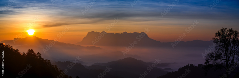 Obraz premium winter sunrise over the misty mountains of northern Thailand, featuring the silhouette of Doi Luang Chiang Dao. The golden light contrasts with the cool, foggy atmosphere, creating a serene landscape.