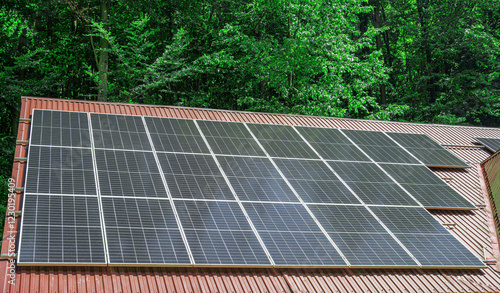 Obraz na płótnie Solar panels installed on a sloped roof surrounded by lush green trees. w salonie