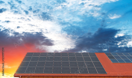 A set of solar panels is installed on the roof of a building with red tiles under a clear blue sky.