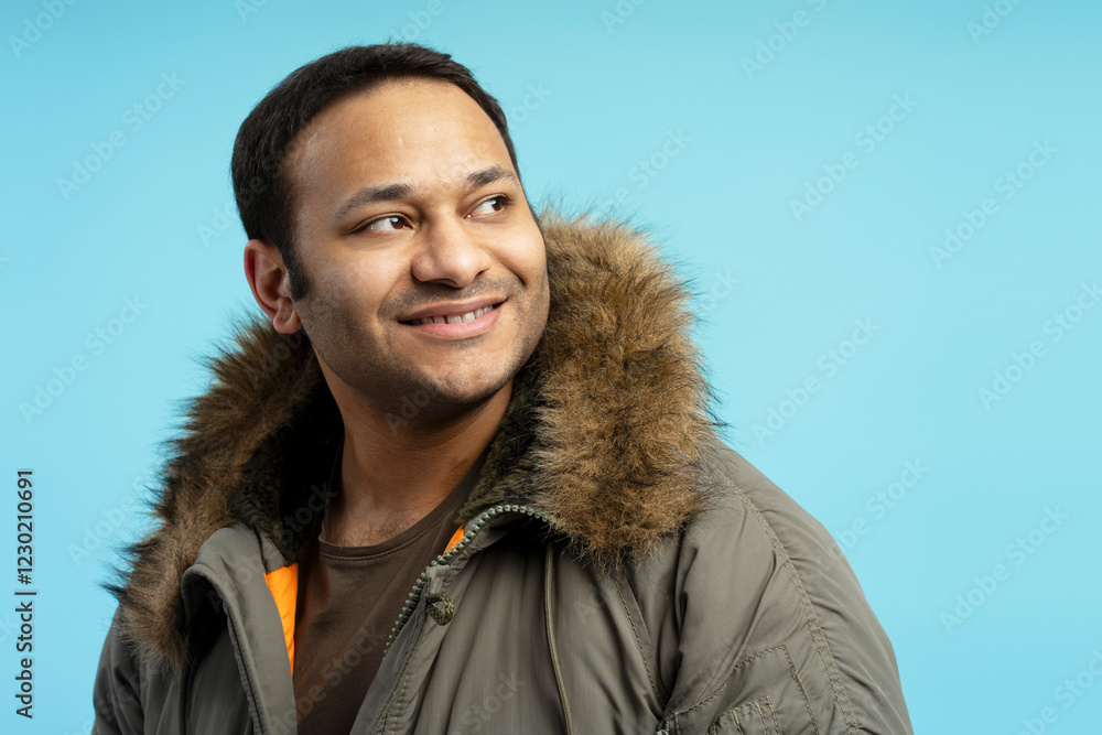 Smiling man wearing winter coat looking away on blue background Smiling man wearing winter coat looking away on blue background