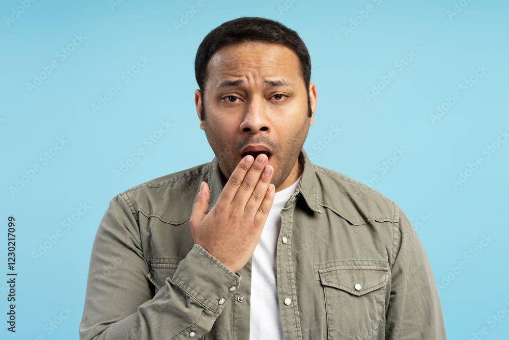 Sleepy man yawning and covering mouth with hand on blue background Sleepy man yawning and covering mouth with hand on blue background
