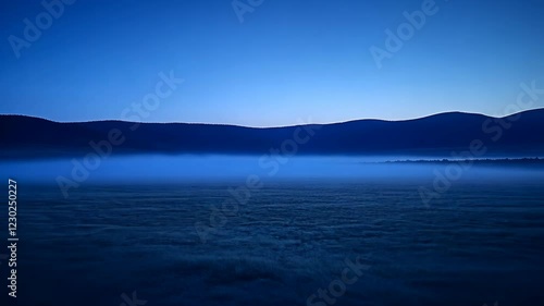 Serene early morning view of mountains reflecting over calm water with soft mist in the distance