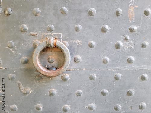 Antique metal gate with rivets and a door handle in the form of a ring. Architectural background with an old wrought iron door in gray. Door knocker.  Copy space photo