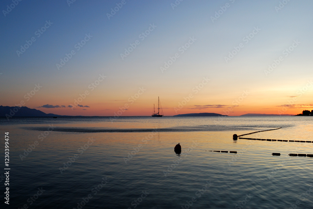 Fototapeta premium Serene sunset over calm waters a sailboat silhouetted against the vibrant sky