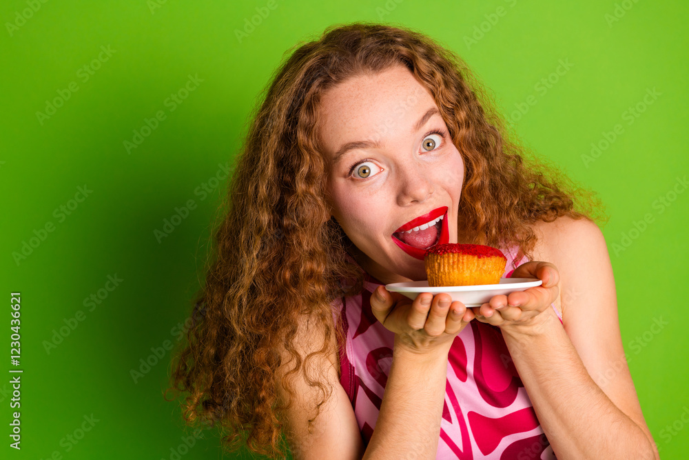 Young woman with curly hair enjoying a cupcake against green background Young woman with curly hair enjoying a cupcake against green background