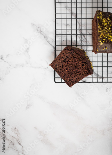 Sliced cake on a cooling rack with a bigger cake on the side. White marble counter as a background