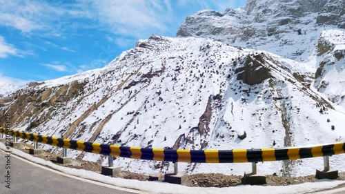 4K shot of snowy Himalayan mountain peak during the sunny day with clouds against the blue sky as seen during the winter seasons at Keylong in Lahaul and Spiti district, Himachal Pradesh, India. photo