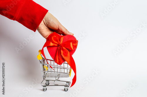 A female hand lays out a gift red box in a shopping basket on a white background.