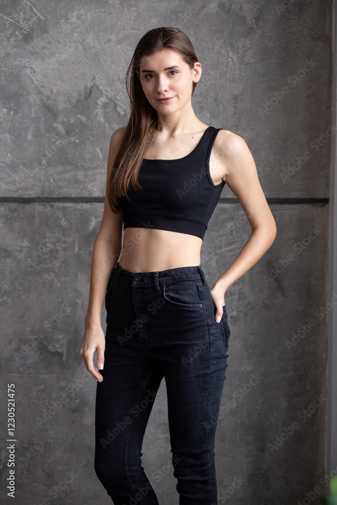 A professional modeling snapshot of a young female model in a black crop top and high-waisted jeans, posing against a textured gray wall. Capturing her natural elegance, toned physique, and confident A professional modeling snapshot of a young female model in a black crop top and high-waisted jeans, posing against a textured gray wall. Capturing her natural elegance, toned physique, and confident